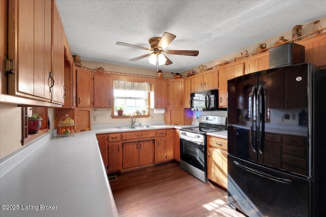 kitchen featuring ceiling fan, wood finished floors, a sink, light countertops, and black appliances