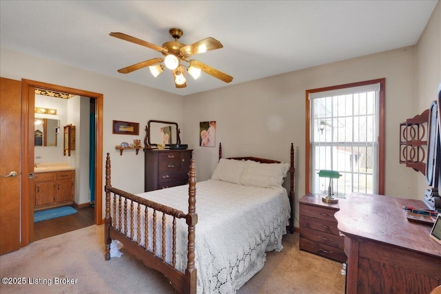 bedroom with a ceiling fan, light colored carpet, and ensuite bath