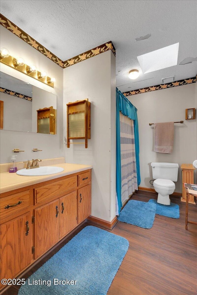 bathroom with toilet, a skylight, a textured ceiling, and wood finished floors