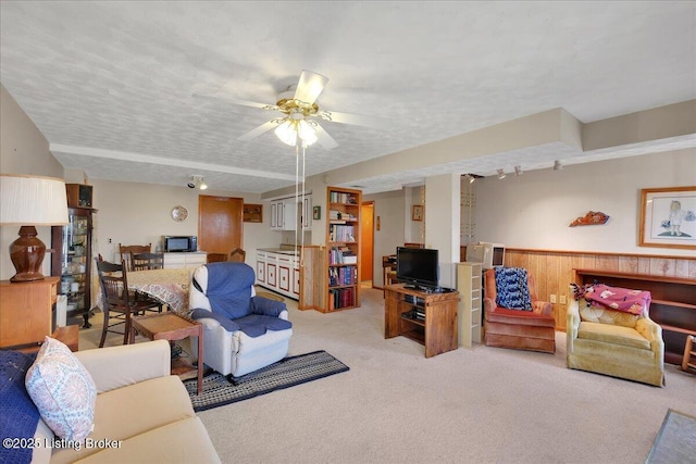 living room featuring carpet, a ceiling fan, a textured ceiling, and wainscoting