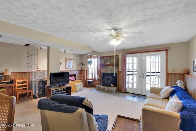 carpeted living room featuring ceiling fan, a textured ceiling, wooden walls, a wainscoted wall, and french doors