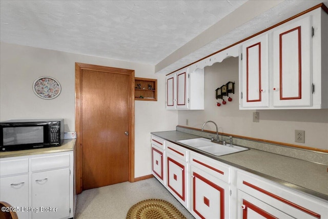 kitchen with a textured ceiling, black microwave, white cabinets, and a sink