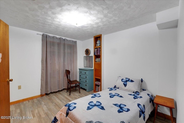 bedroom featuring light wood-style flooring, baseboards, and a textured ceiling