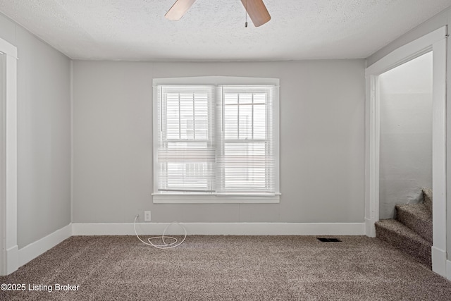 carpeted spare room featuring baseboards, ceiling fan, visible vents, and a textured ceiling