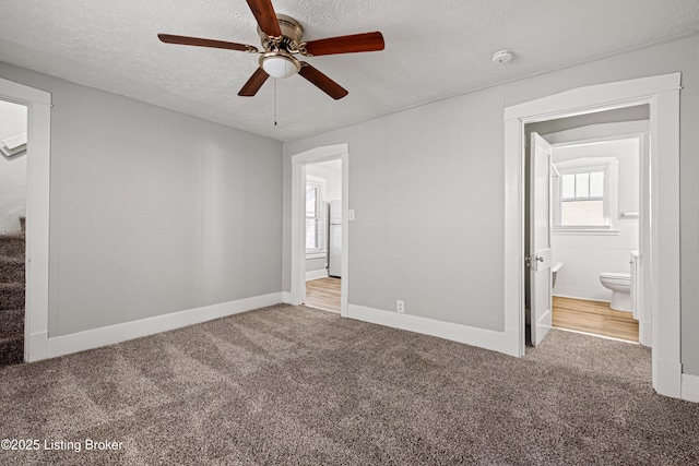 unfurnished bedroom with a textured ceiling, carpet, ensuite bath, and freestanding refrigerator