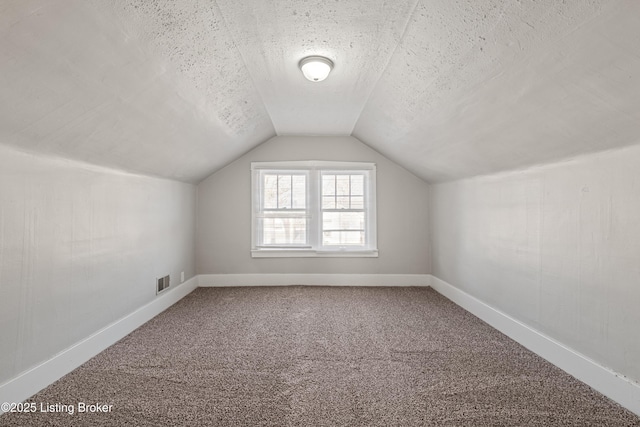 additional living space with carpet, visible vents, vaulted ceiling, and a textured ceiling