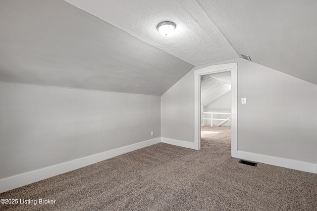 additional living space with carpet, visible vents, a textured ceiling, and baseboards