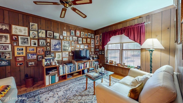 living area featuring wood walls, a ceiling fan, and crown molding