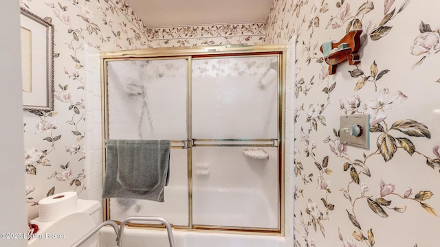 bathroom featuring combined bath / shower with glass door, toilet, and wallpapered walls