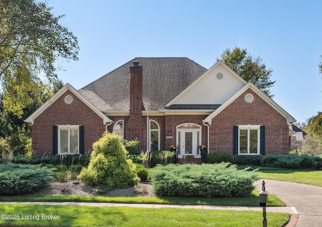 view of front of property featuring roof with shingles, brick siding, and a chimney