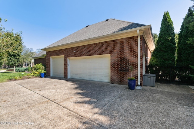 view of side of property with a garage, a shingled roof, concrete driveway, and brick siding