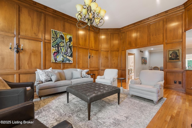 living area featuring light wood-style flooring, wooden walls, a decorative wall, an inviting chandelier, and crown molding