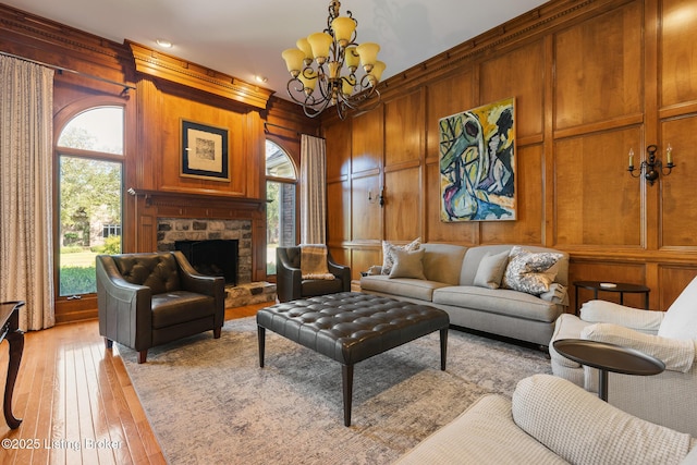 living area with a stone fireplace, wooden walls, a decorative wall, a notable chandelier, and light wood finished floors