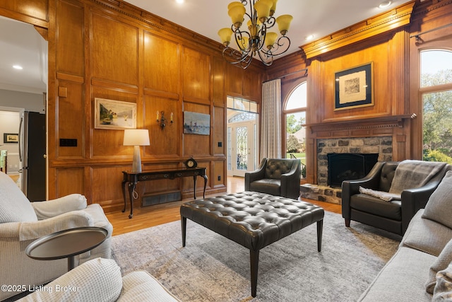 living room with light wood-style flooring, ornamental molding, wood walls, a stone fireplace, and a chandelier