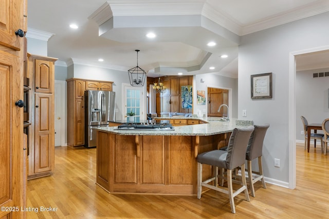 kitchen featuring a breakfast bar area, stainless steel appliances, a sink, visible vents, and light stone countertops