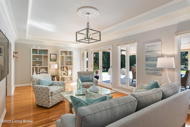 living room featuring baseboards, ornamental molding, wood finished floors, a tray ceiling, and french doors