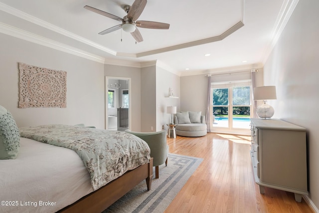 bedroom featuring a tray ceiling, crown molding, a ceiling fan, ensuite bath, and light wood-type flooring