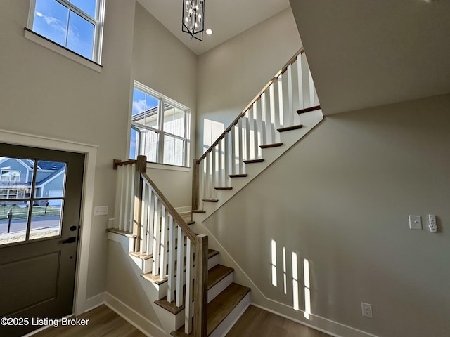 staircase featuring a chandelier, baseboards, a high ceiling, and wood finished floors