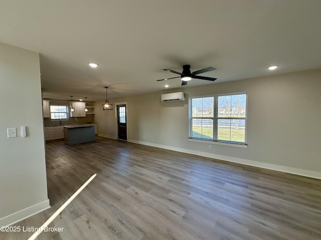 unfurnished living room with a wall unit AC, baseboards, wood finished floors, and recessed lighting