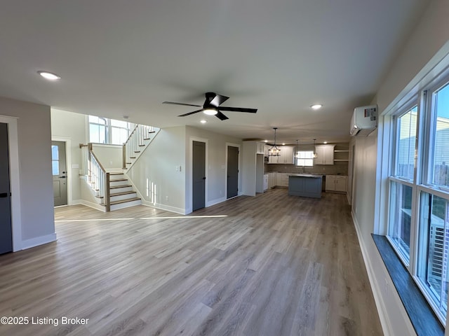 unfurnished living room featuring light wood-style floors, an AC wall unit, stairway, and baseboards