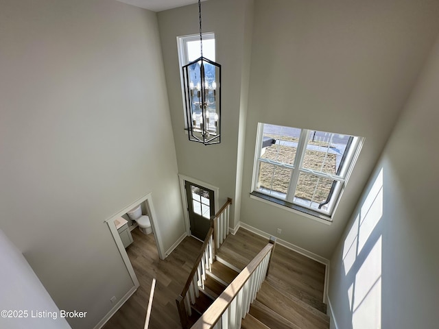 staircase featuring baseboards, a high ceiling, a chandelier, and wood finished floors