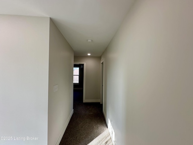 hallway featuring dark colored carpet and baseboards