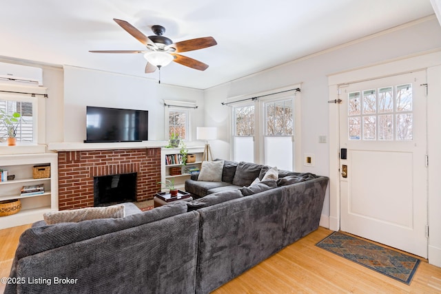 living room with light wood-type flooring, a fireplace, a ceiling fan, and a wall mounted AC