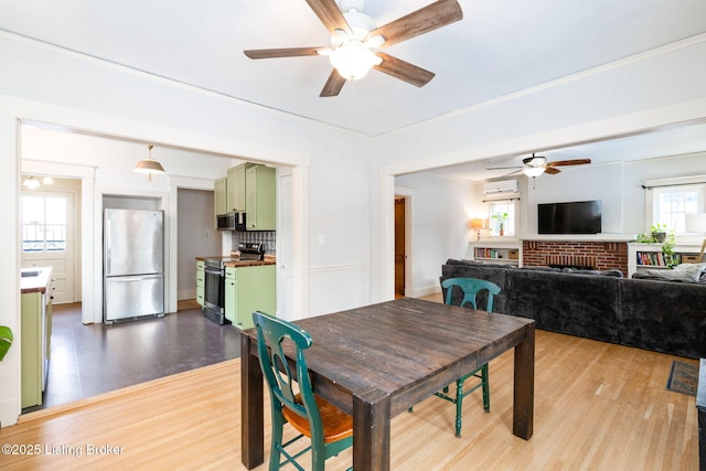 dining area featuring a fireplace, a ceiling fan, wood finished floors, and a wall mounted AC