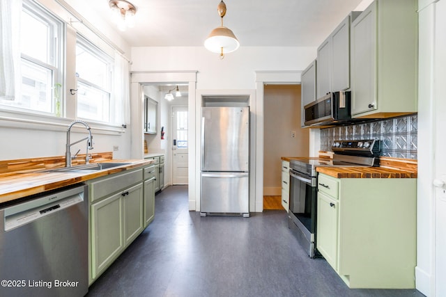 kitchen with stainless steel appliances, decorative backsplash, green cabinets, a sink, and butcher block countertops