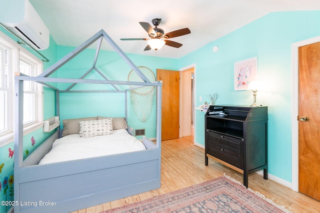 bedroom with baseboards, visible vents, lofted ceiling, wood finished floors, and a wall mounted AC