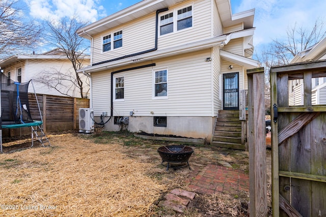 back of house featuring a fire pit, a trampoline, fence, and ac unit