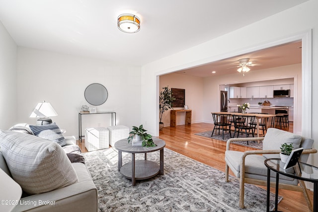 living area featuring light wood-style floors, baseboards, and a ceiling fan