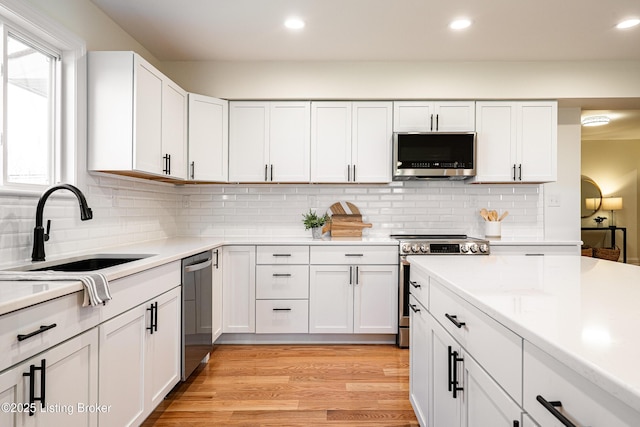 kitchen featuring a sink, white cabinetry, light countertops, appliances with stainless steel finishes, and light wood-type flooring