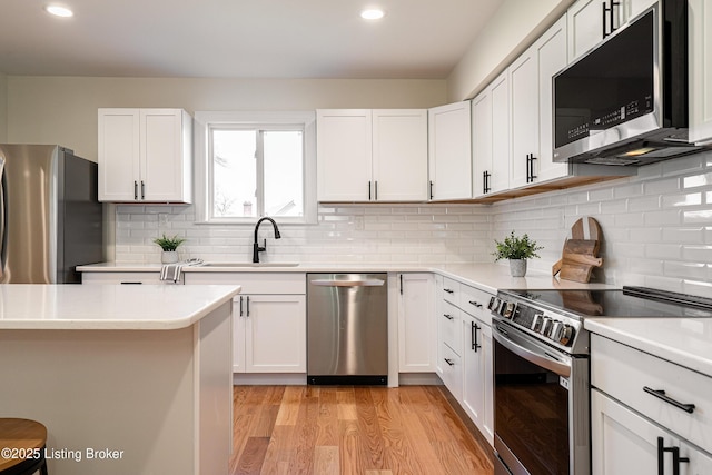 kitchen featuring stainless steel appliances, light wood finished floors, a sink, and light countertops