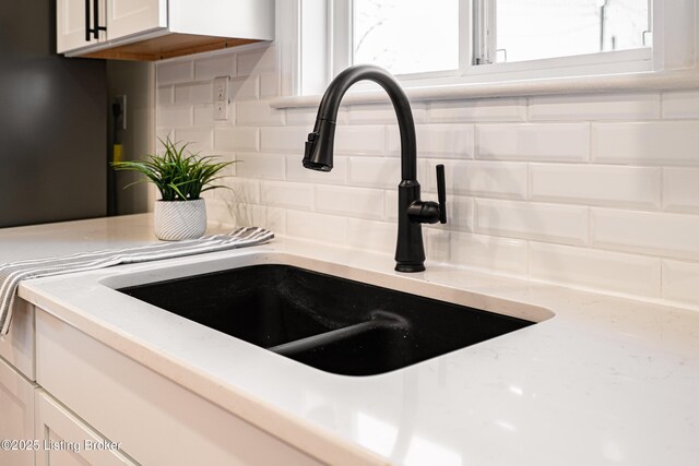 room details with light stone countertops, tasteful backsplash, white cabinetry, and a sink