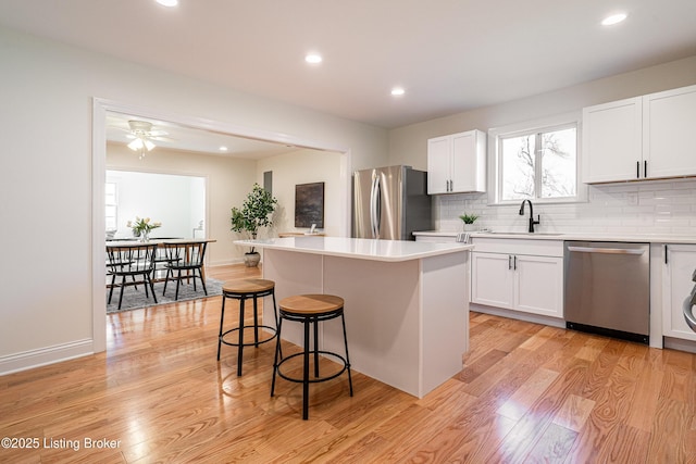 kitchen featuring light wood-style flooring, appliances with stainless steel finishes, a sink, a kitchen bar, and backsplash