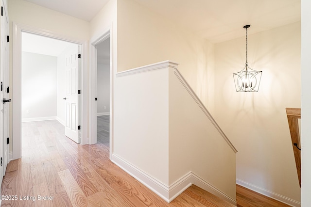 corridor featuring a chandelier, light wood-style flooring, and baseboards