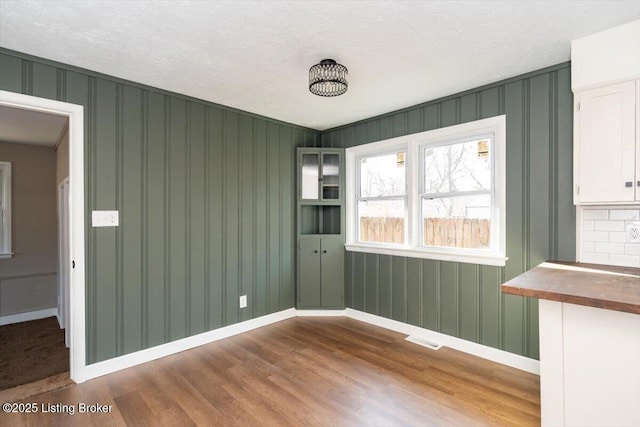 unfurnished room with a textured ceiling, wood finished floors, visible vents, and baseboards