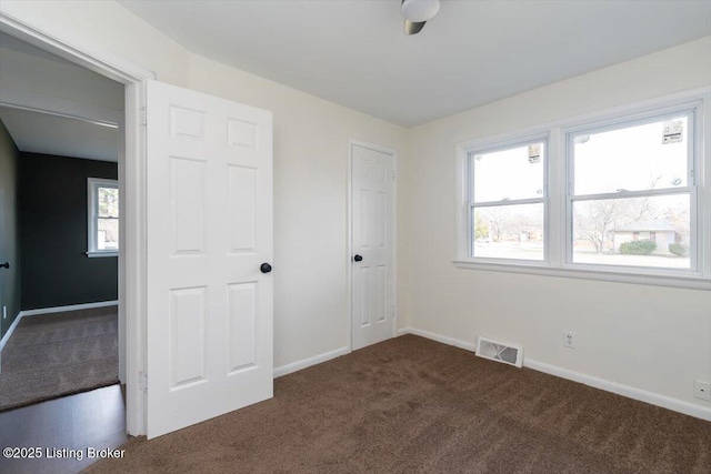 unfurnished bedroom with dark colored carpet, visible vents, and baseboards