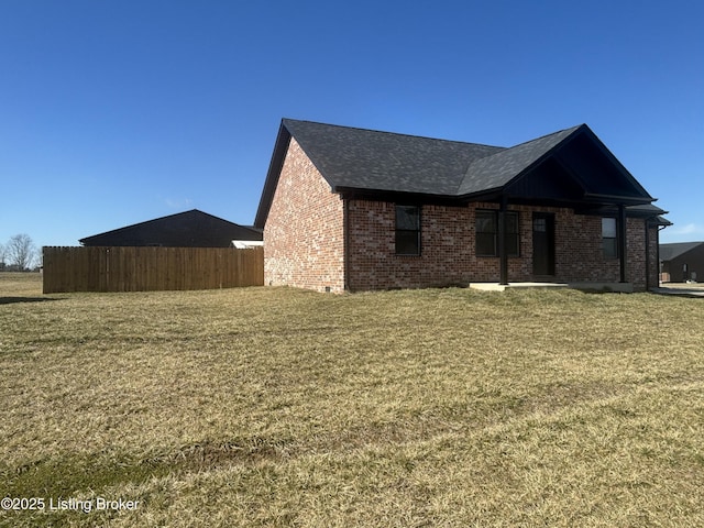 view of side of property featuring brick siding, roof with shingles, fence, and a yard