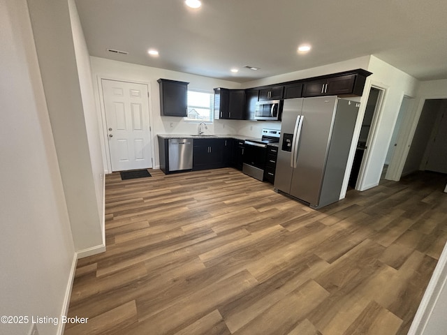 kitchen with recessed lighting, stainless steel appliances, wood finished floors, a sink, and light countertops