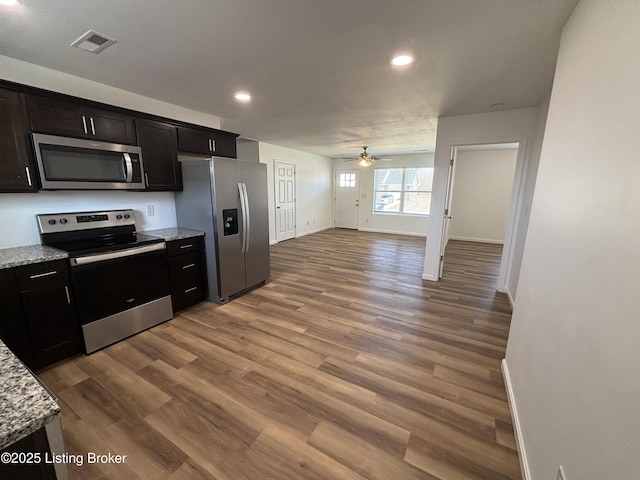 kitchen featuring visible vents, ceiling fan, light stone counters, appliances with stainless steel finishes, and wood finished floors