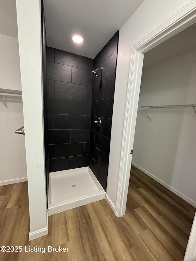 bathroom with a spacious closet, a stall shower, wood finished floors, and baseboards