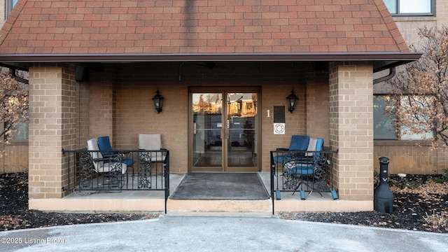 doorway to property with a patio area, a shingled roof, french doors, and brick siding