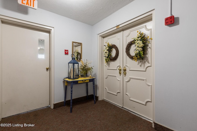 foyer entrance featuring dark colored carpet and a textured ceiling