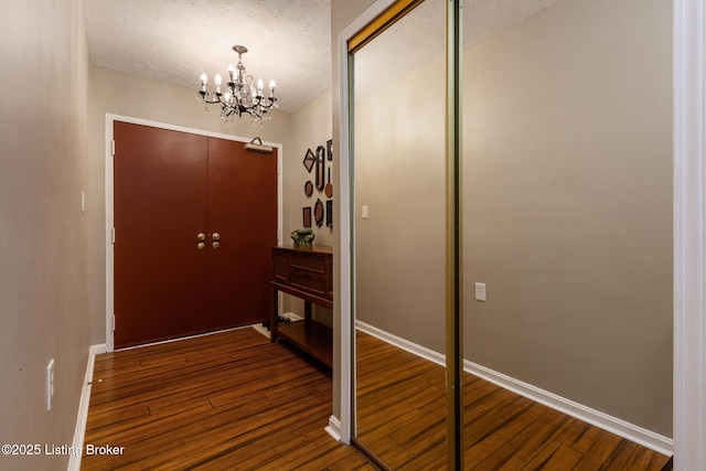 doorway featuring a notable chandelier, a textured ceiling, baseboards, and hardwood / wood-style floors