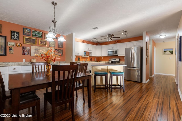 dining room featuring visible vents, dark wood-type flooring, ceiling fan, a textured ceiling, and baseboards