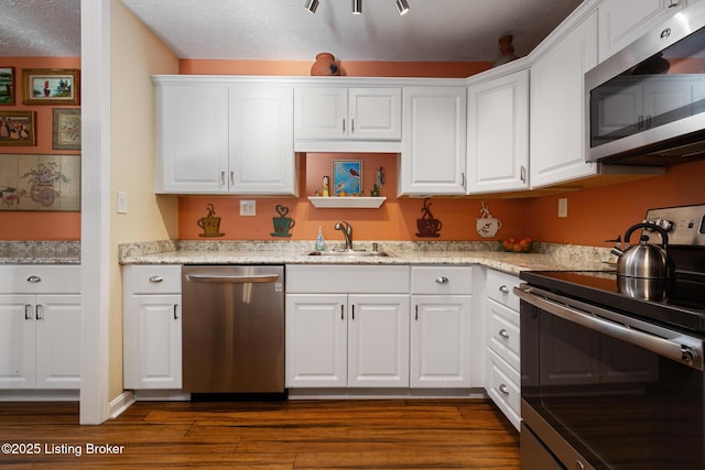 kitchen with dark wood-style floors, stainless steel appliances, white cabinetry, a sink, and a textured ceiling