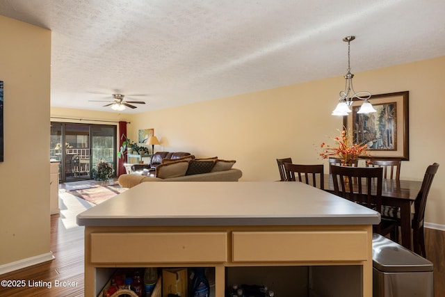 kitchen featuring light countertops, hanging light fixtures, dark wood-type flooring, a textured ceiling, and ceiling fan with notable chandelier