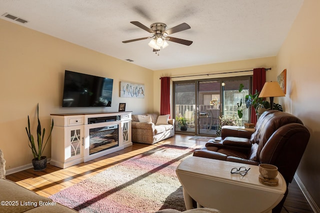 living room with ceiling fan, wood finished floors, visible vents, and baseboards